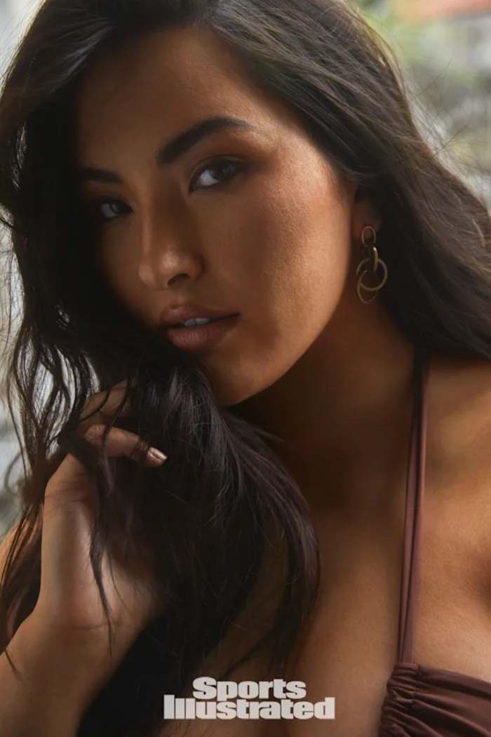 Yumi Nu poses with a hand in her dark brown hair, wearing a brown bikini top.